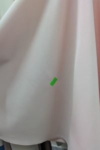 Na jasnoróżowej tkaninie przyklejono mały zielony kawałek taśmy, który zaznacza miejsce na materiale — oznacza to, że ta sukienka „Bokserka” pochodzi z naszej kolekcji OUTLET i jest sklasyfikowana jako II gatunek.