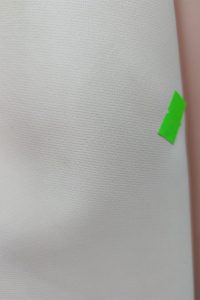 Na gładkiej, białej, teksturowanej powierzchni przyklejona jest mała zielona naklejka z napisem „OUTLET”.