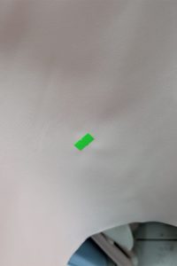 Mały zielony kawałek taśmy, oznaczony jako „II Gatunek”, przyklejony jest do jasnobeżowej powierzchni z lekką zmarszczką.