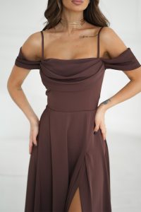 Kobieta ubrana w opadającą ramiączka, brązową sukienkę maxi z rozcięciem, złoty choker i widoczne tatuaże na ramionach.