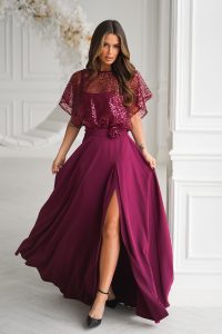 Kobieta w cekinowym topie w kolorze magenta i lejącej spódnicy z rozcięciem na wysokości uda, stylizowanej na elegancką sukienkę, stojąca w białym pokoju.