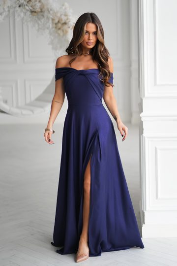 Kobieta w Długiej sukni wieczorowej z dekoltem odkrywającym ramiona i rozcięciem do uda, z subtelnym metalicznym połyskiem, stojąca w pomieszczeniu.