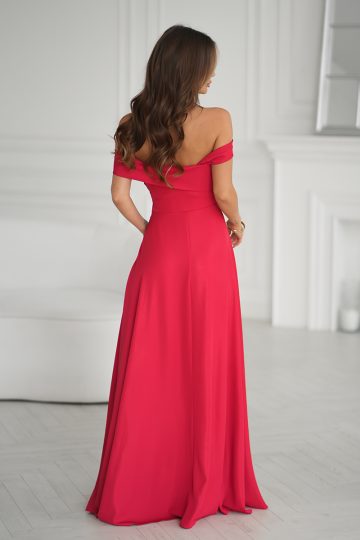 Kobieta w długiej sukni wieczorowej z metalicznym połyskiem stoi w białym pokoju, odwrócona od kamery.