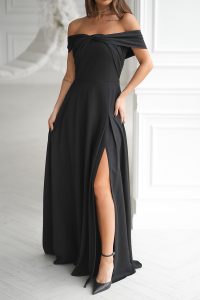 Kobieta ubrana w długą suknię wieczorową z metalicznym połyskiem i rozcięciem na wysokości uda, stojąca w jasnym, eleganckim pomieszczeniu.