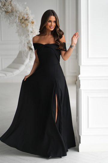 Kobieta w długiej sukni wieczorowej z rozcięciem na ramionach i subtelnym metalicznym połyskiem, stojąca w jasnym, eleganckim białym pokoju.