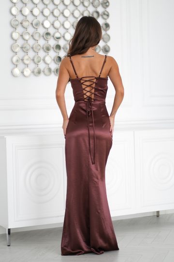 Kobieta w długiej sukni z gorsetowym sznurowaniem, stojąca w pomieszczeniu i odwrócona od kamery.