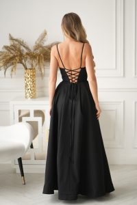 Kobieta w czarnej, sięgającej podłogi Długiej Sukni Wieczorowej bez pleców z Gorsetowym Sznurowaniem, stojąca w białym, eleganckim pomieszczeniu. Model 341-06.