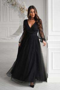 Kobieta w długiej czarnej tiulowej sukience z przezroczystymi rękawami, stojąca w jasnym, eleganckim białym pokoju.
