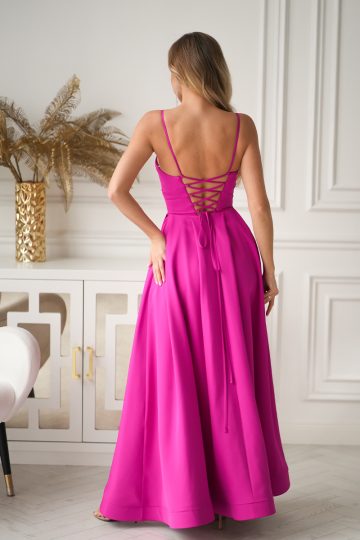 Kobieta w jasnoróżowej Długiej Sukni Wieczorowej, 341-07, z Gorsetowym Sznurowaniem z tyłu stoi w eleganckim pokoju, odwrócona tyłem.