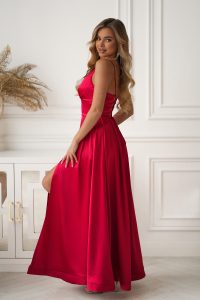 Kobieta w długiej, eleganckiej czerwonej sukience pozuje w jasnym, stylowym pomieszczeniu o białych ścianach i jasnym wystroju.