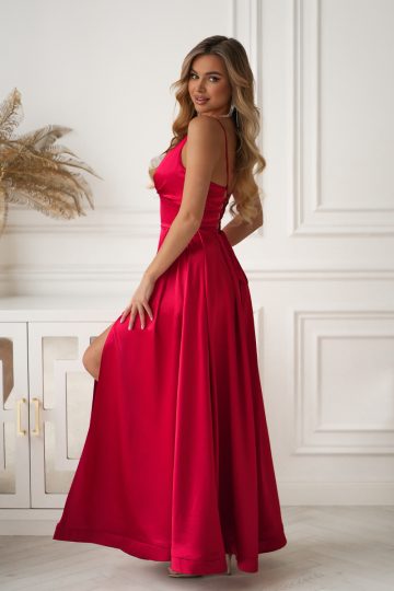 Kobieta w długiej, eleganckiej czerwonej sukience pozuje w jasnym, stylowym pomieszczeniu o białych ścianach i jasnym wystroju.