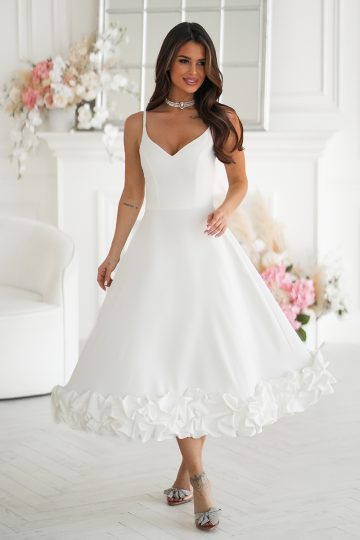 Kobieta w sukience midi ecru z kwiatowym wykończeniem, stojąca z gracją w eleganckim pokoju ozdobionym świeżymi kwiatami.