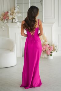 Kobieta w jasnoróżowej sukni bez pleców stoi w białym pokoju z kwiatami i eleganckim wystrojem.