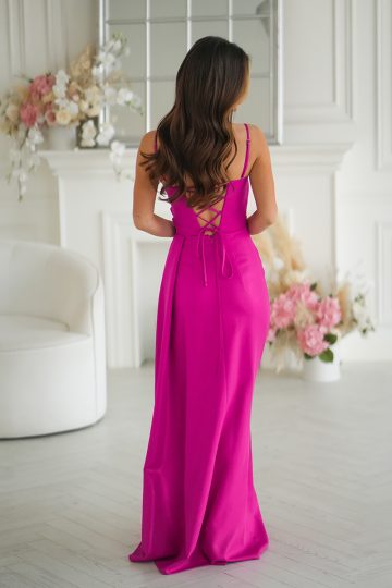 Kobieta w jasnoróżowej sukni bez pleców stoi w białym pokoju z kwiatami i eleganckim wystrojem.