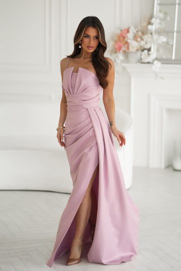 Kobieta w długiej, jasnoróżowej sukni wizytowej z rozcięciem na wysokości uda, stojąca w jasnym, eleganckim pomieszczeniu.