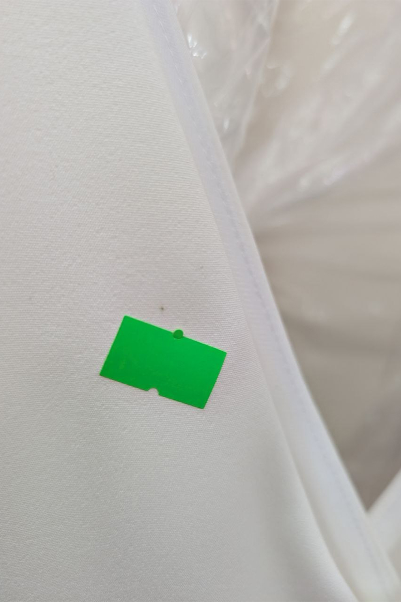 Mała zielona naklejka na białej, teksturowanej powierzchni z szwem i przezroczystym plastikiem w tle, przywodząca na myśl wyrafinowaną estetykę charakterystyczną dla „Eleganckiej Dopasowanej Sukienki”. Mała zielona naklejka na białej, teksturowanej powierzchni z szwem i przezroczystym plastikiem w tle, przywodząca na myśl wyrafinowaną estetykę charakterystyczną dla „Eleganckiej Dopasowanej Sukienki”.