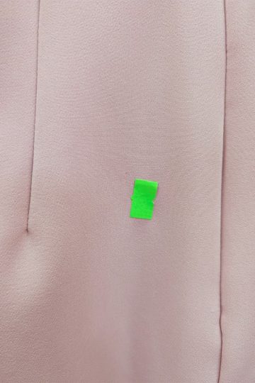 Mały kawałek zielonej taśmy przyklejony jest do jasnoróżowej tkaniny, a po lewej stronie widać szew, co sugeruje, że może to być fragment różowej sukienki.