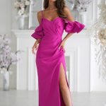 Kobieta w magentaowej sukni z odkrytymi ramionami i rozcięciem sięgającym do uda, stojąca w eleganckim białym pokoju.