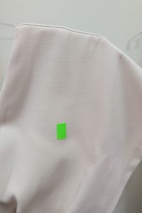 Zbliżenie na jasnoróżową tkaninę z małą zieloną prostokątną naklejką, idealne do zaprezentowania beżowego kombinezonu z serii OUTLET.