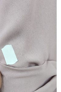 Do jasnoróżowej tkaniny, podobnej do tej użytej w „Sukience z marszczeniem”, przyklejono kawałek białej taśmy; w pobliżu widoczna jest niewielka dziurka lub zaciągnięcie.