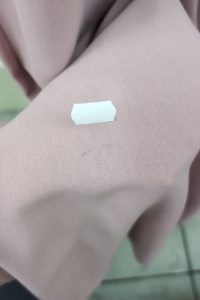 Mała biała naklejka na jasnoróżowej tkaninie Sukienka Maxi z marszczeniem w talii, na tle podłogi wyłożonej płytkami.