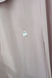 Na jasnoróżowej tkaninie przyklejona jest mała biała naklejka, pod którą widać wgniecenie, co sugeruje, że może to być fragment sukienki maxi z marszczeniem w talii.