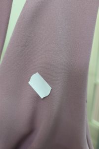 Mała biała naklejka na gładkiej, fioletowo-różowej powierzchni tkaniny, przypominająca „Długą Różową Sukienkę”, którą można znaleźć w sklepie „Sukienka Outlet”.