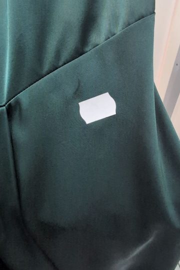 Kawałek białej taśmy przyklejono do ciemnozielonej tkaniny z widocznymi szwami, co przypomina luksusową sukienkę satynową.