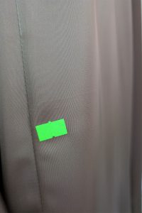 Zbliżenie na szarą tkaninę z małą, prostokątną zieloną naklejką przyklejoną do jej powierzchni, przypominającą gładką fakturę charakterystyczną dla sukienki satynowej.