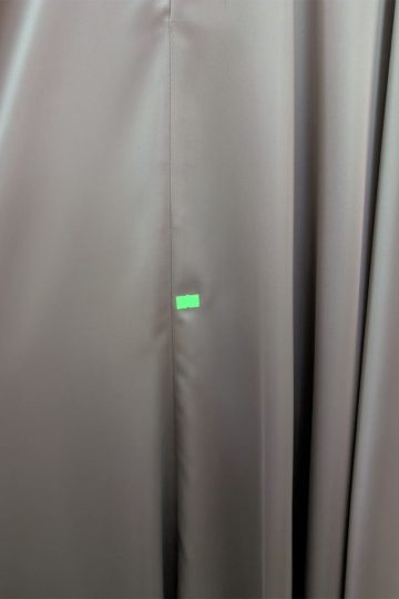 Brązowa tkanina z małą zieloną naklejką w pobliżu środkowego szwu, przypominająca odcień cappuccino. Powierzchnia wydaje się gładka i lekko błyszcząca, co przywodzi na myśl luksusowy charakter satynowej sukienki.